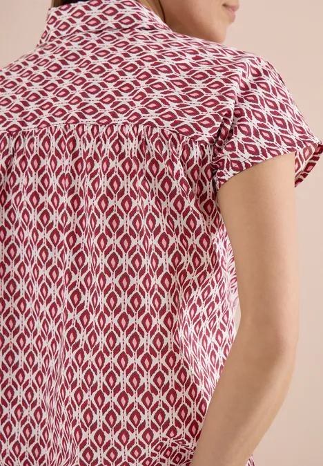 Rückansicht einer Frau mit roter, weißer, geometrisch gemusterter Kurzarmbluse.